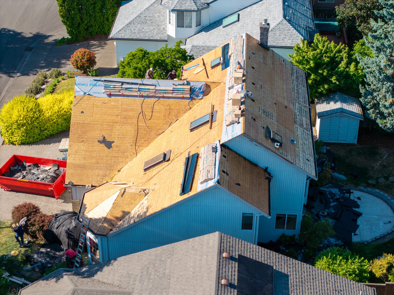 Aerial view of an Evolution RoofWorks roof replacement on an early-2000s Hillsboro, Oregon home, with the old shingles torn off to new decking, skylights being reflashed, and a debris trailer in the driveway