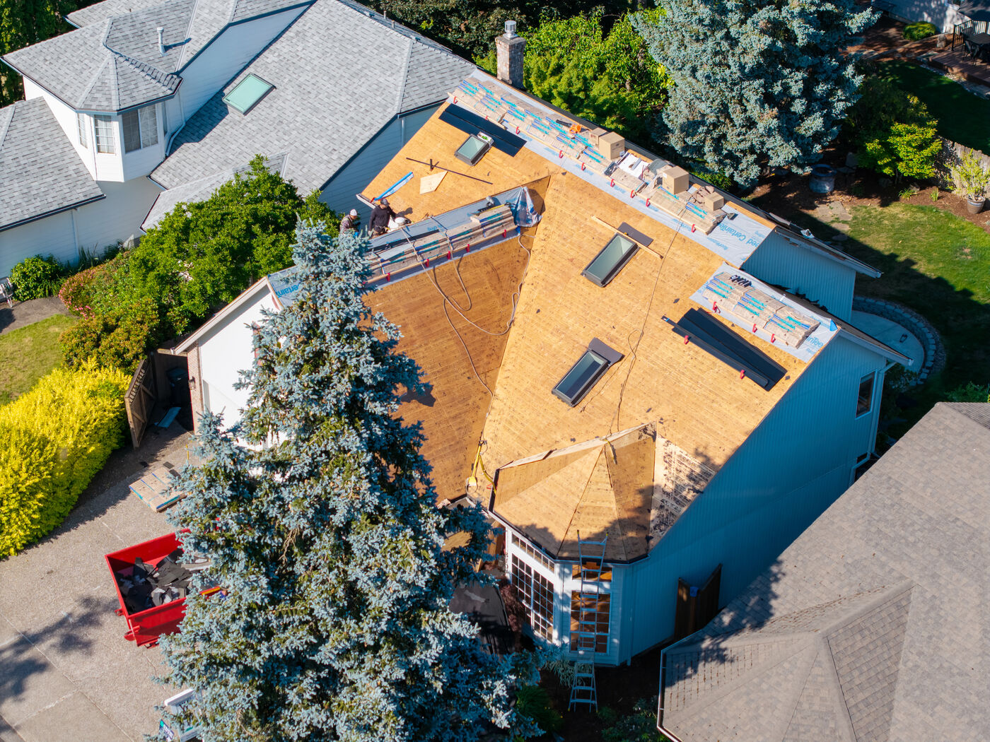 Aerial view of an Evolution RoofWorks roof replacement in progress, with the old shingles torn off to bare decking, new shingle bundles staged along the ridge, and similar neighboring homes