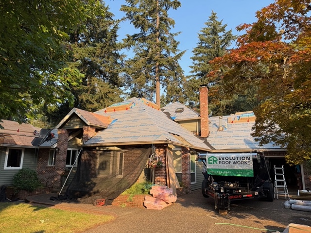Evolution RoofWorks crew mid-replacement on a Tualatin home, with new plywood decking and synthetic underlayment installed and debris netting protecting the house